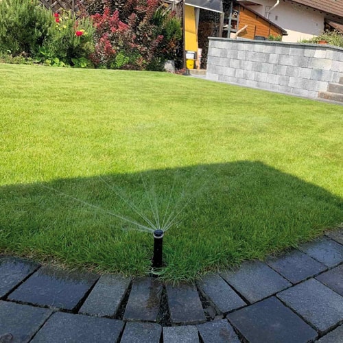 Präzise installierter Versenkregner bei der Bewässerung einer Rasenkante im Privatgarten