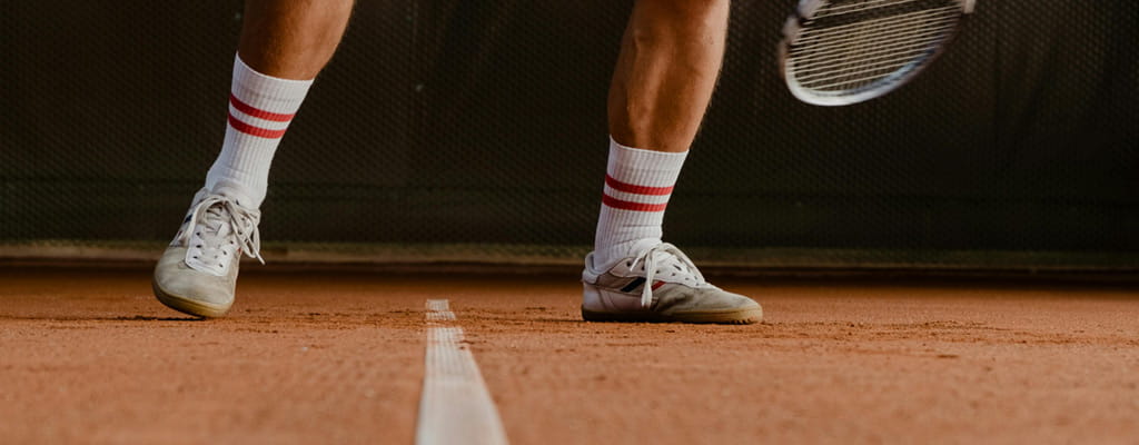 Dynamische Nahaufnahme eines Tennisspielers beim Slide auf Ziegelmehl zur Verdeutlichung der notwendigen Bodenhaftung durch professionelle Bewässerung
